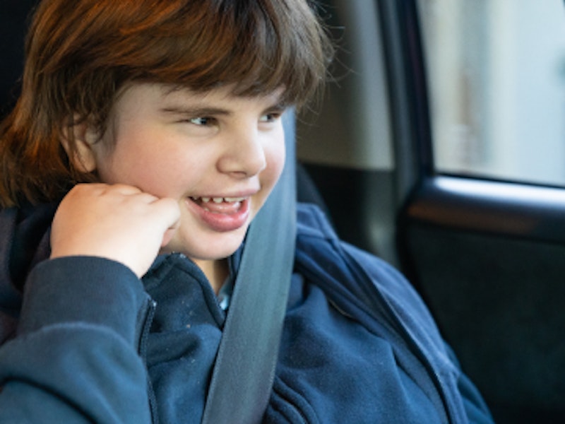 Smiling girl with disability wearing a seatbelt in the back seat of the family car